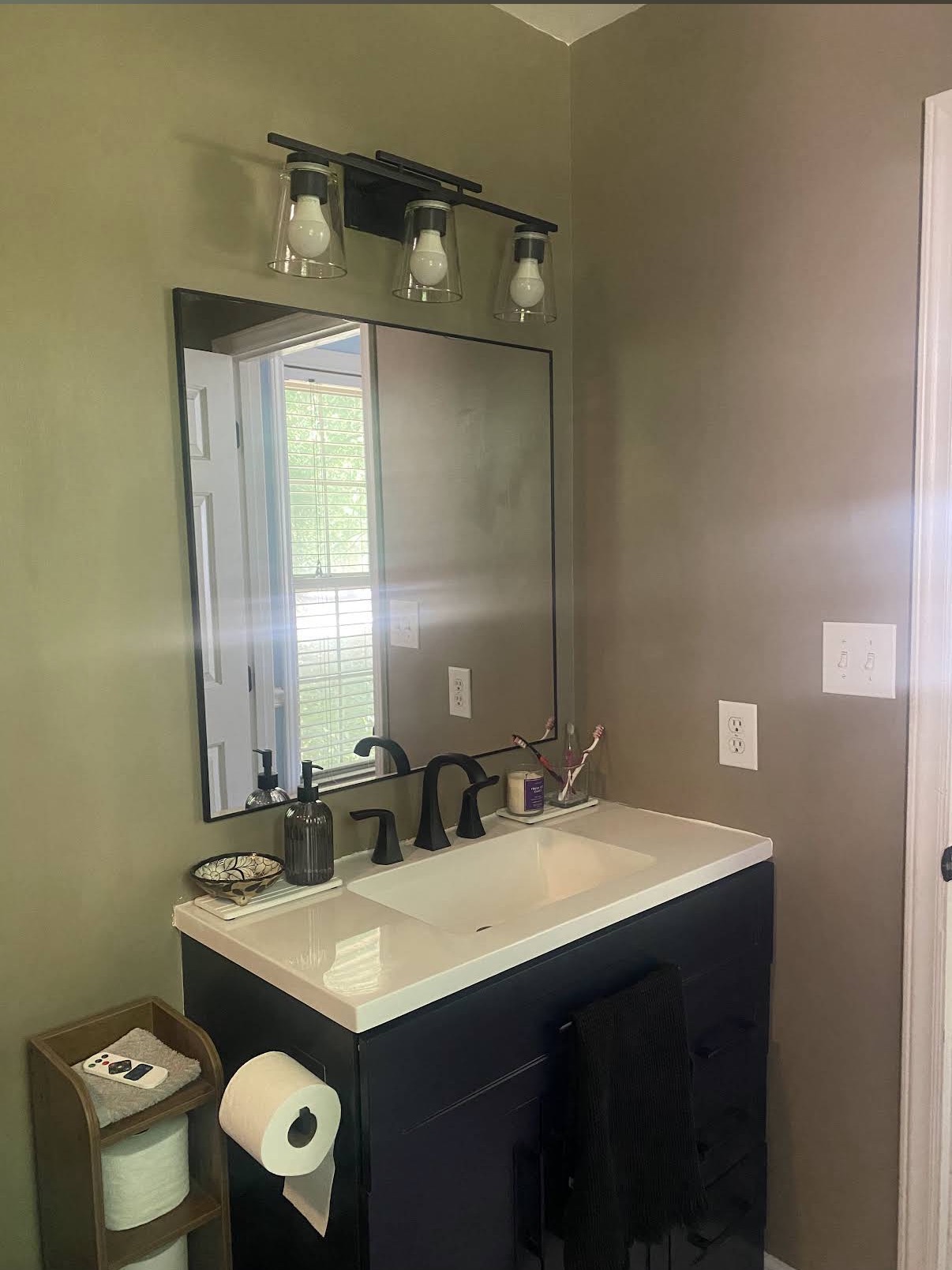 Dark bathroom vanity with white countertop, black faucet, rectangular mirror and three-light fixture