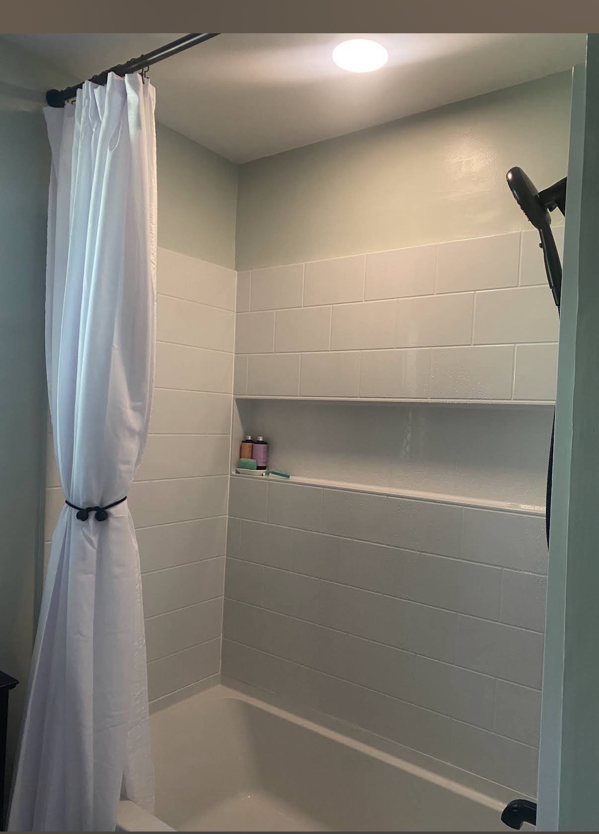 White shower surround with a wide recessed storage niche and black showerhead